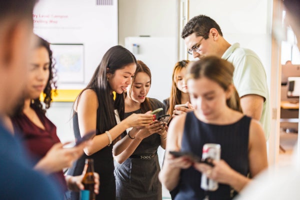 Six people huddle around their phones in a conference room.
