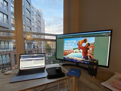 A picture of Katie McGahan’s desk with a Ford mug and notebook, her laptop open and a computer monitor on showing a Ford advertisement
