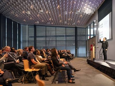 A man speaking on stage in front of a large room filled with people.
