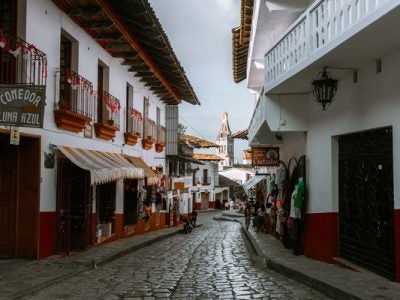 A narrow, cobblestone street featuring red and white buildings and business signs in Spanish.
