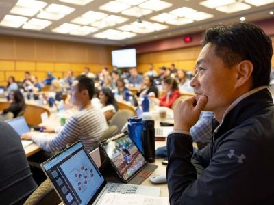 H1-B student sitting in a large university lecture hall with a laptop open in front of them