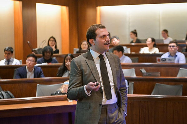 A man in a business suit standing and addressing an audience in an auditorium.