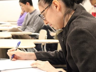 A student sits writing at a desk with a pen and paper.
