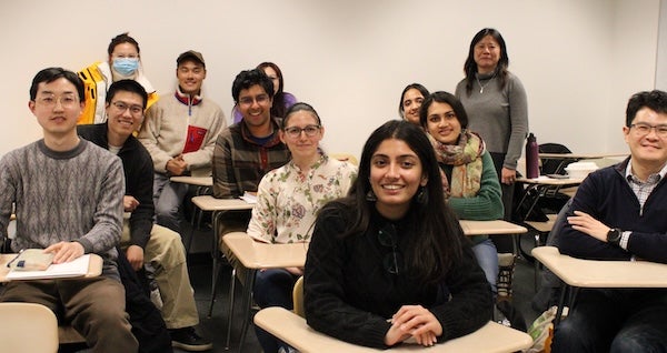 Students sit at desks and smile at the camera.