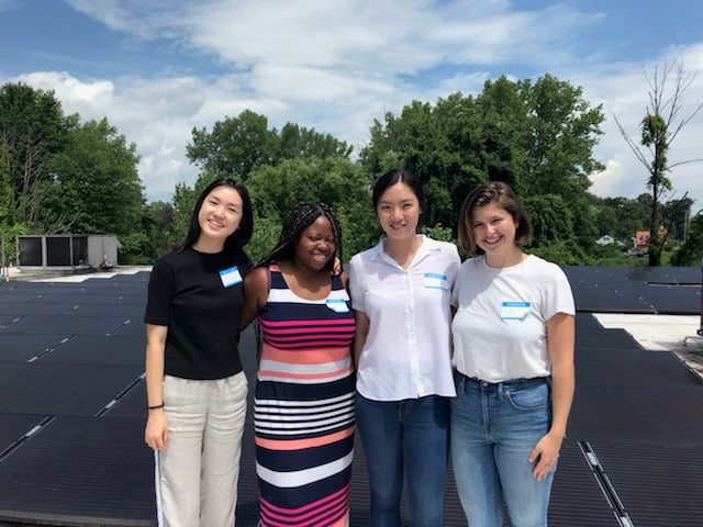 Four women standing on top of solar panels on a roof.