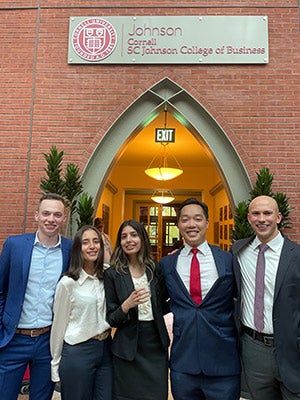 Ian Cairns standing in a row with two men and two women under an SC Johnson College of Business sign.