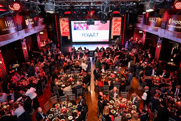 Photo taken from above of a large banquet hall filled with tables and people with a stage at the front of the room.