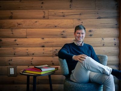 Ilya Brotzky sitting in a chair in front of a wood paneled wall.