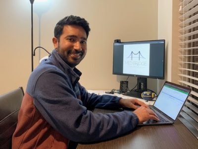 A picture of Rahul Singh sitting at his desk in front of a computer, working from his office