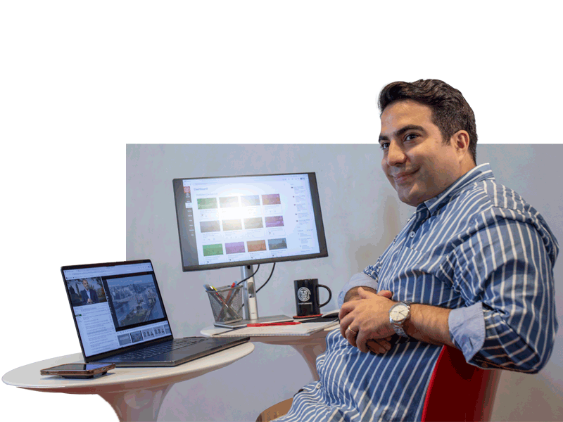 Mid-30's male student at home taking and executive MBA class. Sitting in chair wiht laptop and one monitor with class work on screen.