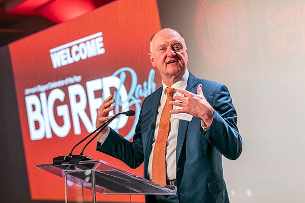 A man gesturing and speaking into a microphone with a "Big Red Bash" banner in the background.