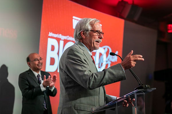 A man speaking into a microphone and gesturing.