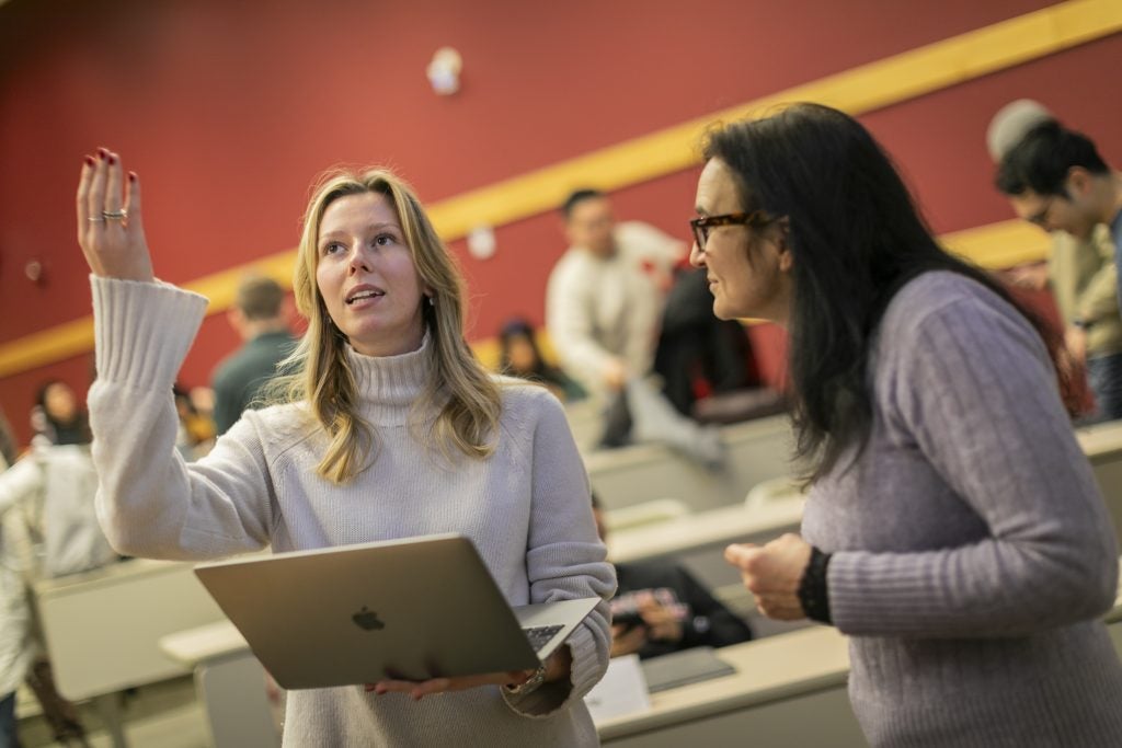 Two women, students enrolled in the Master of Management in Hospitality program at Cornell's Nolan School, collaborate in a lecture hall while standing