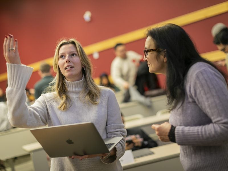 Two women, students enrolled in the Master of Management in Hospitality program at Cornell's Nolan School, collaborate in a lecture hall while standing