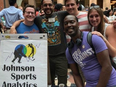 Students stand next to their Johnson Sport Analytics Club sign