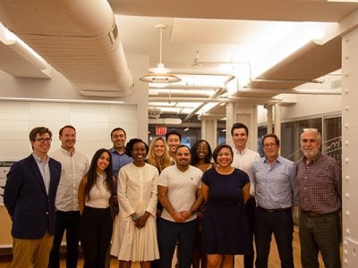 A group of men and women stand together inside a conference room.