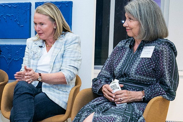 Two women sitting side by side: One is talking intently, looking at the audience and gesturing with both hands, the other is looking on.
