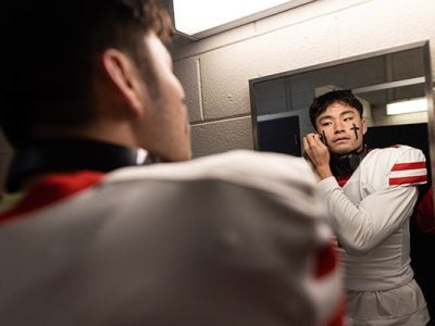 Jameson Wang looking in a mirror and applying eye black in a photo taken from behind and showing his reflection.