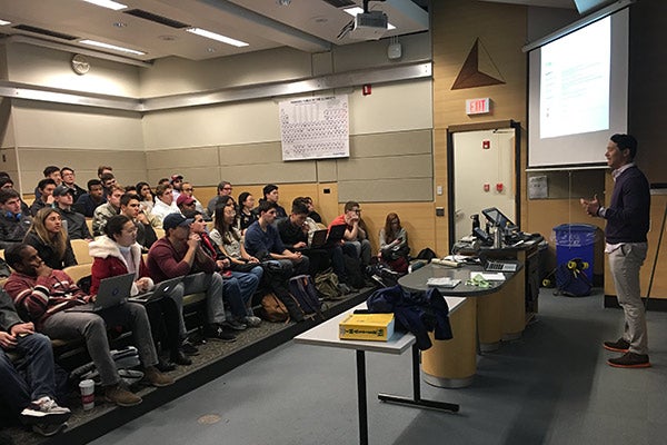 John Wu standing in front of a large class of students and speaking.