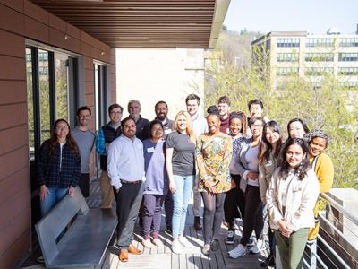Group of students and instructors standing outside on a balcony posing for photo.