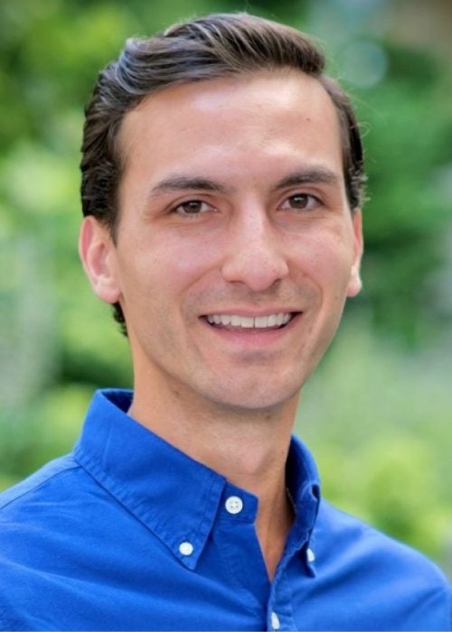 A young man in business attire smiles while out in nature as part of the Cornell MBA program at the Johnson School