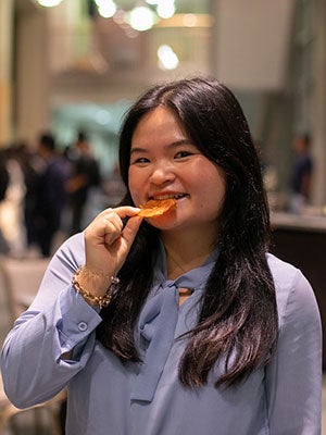 A woman holding a round slice of an orange dried fried up to her mouth and smiling.