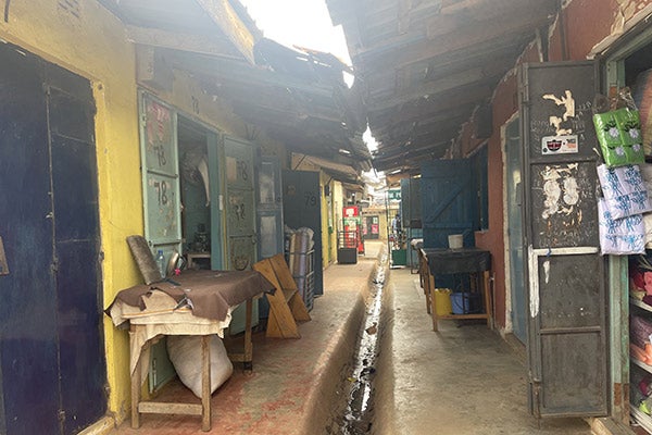 a narrow passage overhung by an uneven roof with well-worn, open shop doors on either side of a concrete walkway with a narrow concrete running down the middle.