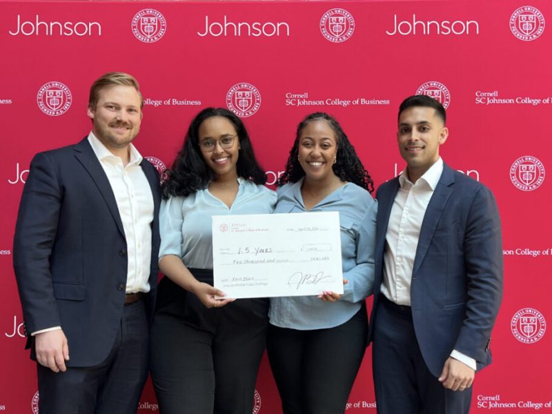 Cornell leadership crisis challenge winners stand in business casual attire against a red and white backdrop and holding a giant prize check