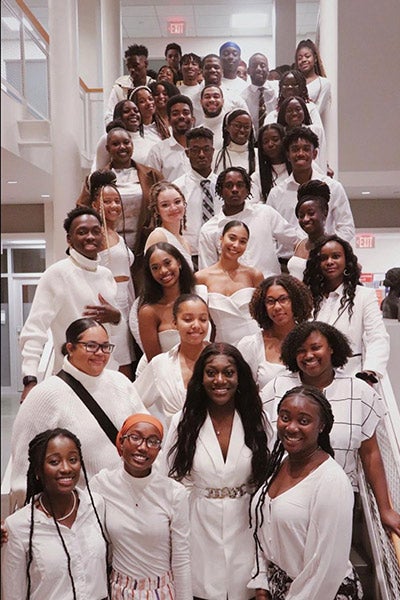 a large group of male and female students standing on a staircase, all dressed in white.