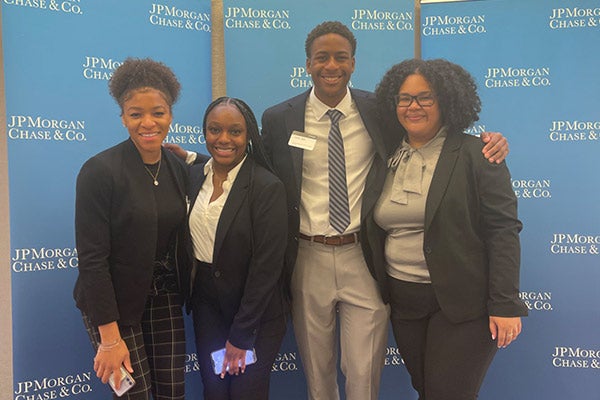 Melanie Abreu with 3 other people dressed in business attire, standing in front of a JP Morgan Chase & Co. backdrop.
