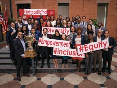 A group of Consortium students stand with their trophy and large signs like #inclusion