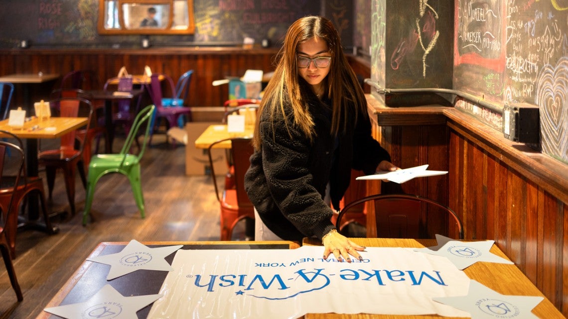Image of female student setting up for a &ldquo;Paint and Sip&rdquo; event at Collegetown Bagels in Ithaca, to raise money for Make-A-Wish Central New York.
