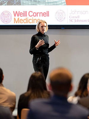 A woman gesturing and speaking on stage with the audience in the foreground.