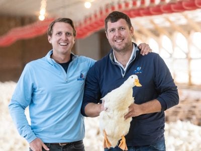 Two men, one holding a large white duck, smile.