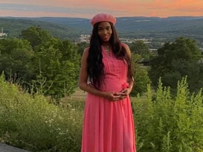 Nichele Nivens standing at the top of a hill with trees and shrubs, a valley, and hills in the background.