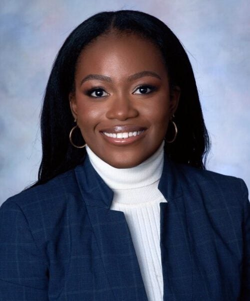 A young woman smiles in business casual attire against a blue background as part of the Cornell MBA program at the Johnson School