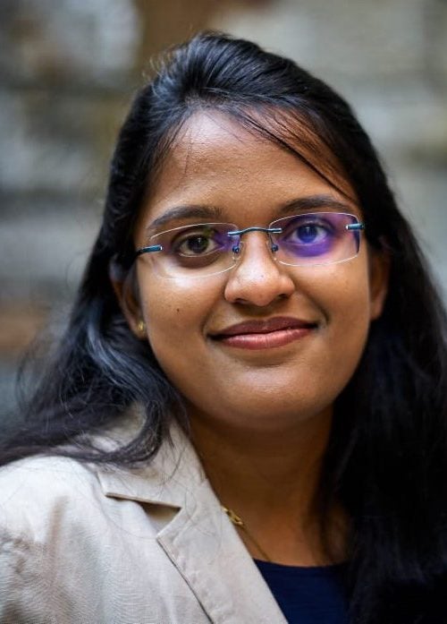 Nithya Kocherlakota, MBA &rsquo;24 looking at the camera in business casual attire, outdoors near an out-of-focus stone wall