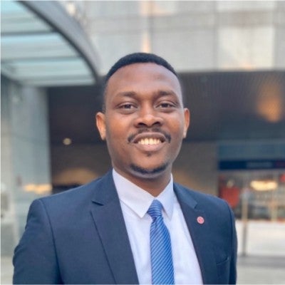 Nnamdi Iwuji, a Cornell MBA Class of 2021 dressed in business formal attire in a contemporary office setting, smiles facing the camera