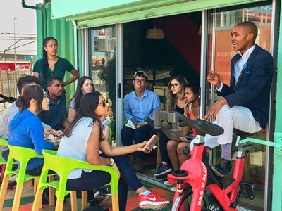 Image of Cornell students from the spinach and lavender SMART teams, both led by Ed Mabaya, meet with Spinach King Lufefe Nomjana (right) outside his Cape Town café. (Credit: Global Cornell)