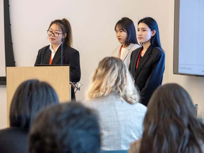 Three female students at a podium presenting in a classroom.