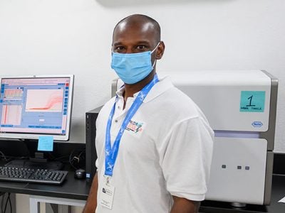 Pradeep Ambrose standing in a lab in front of lab equipment on a counter behind him