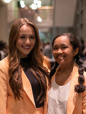 Two women in matching orange suits standing side by side and smiling.