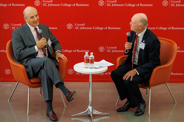 Two men sitting in orange armchairs and speaking into microphones; Andrew Karolyi is looking at Eduardo Padilla Silva, who is looking at the audience.