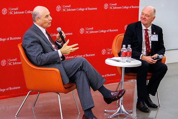 Two men sitting in orange armchairs; Eduardo Padilla Silva is speaking into a microphones while Andrew Karolyi looks on.