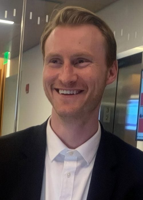 Patrick McNamara, MBA &rsquo;24, a Cornell MBA student in business casual attire, smiling in a glass-enclosed huddle room at Breazzano Family Center at the Cornell SC Johnson College of Business