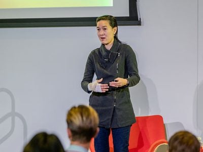 A woman on stage gesturing and speaking.