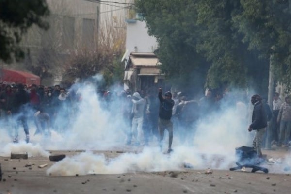 Smoke and large crowds protesting among rubble
