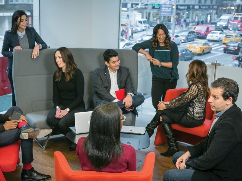 Several Cornell Executive MBA students meet in a contemporary lobby overlooking the busy streets of Manhattan in New York City via large glass walls