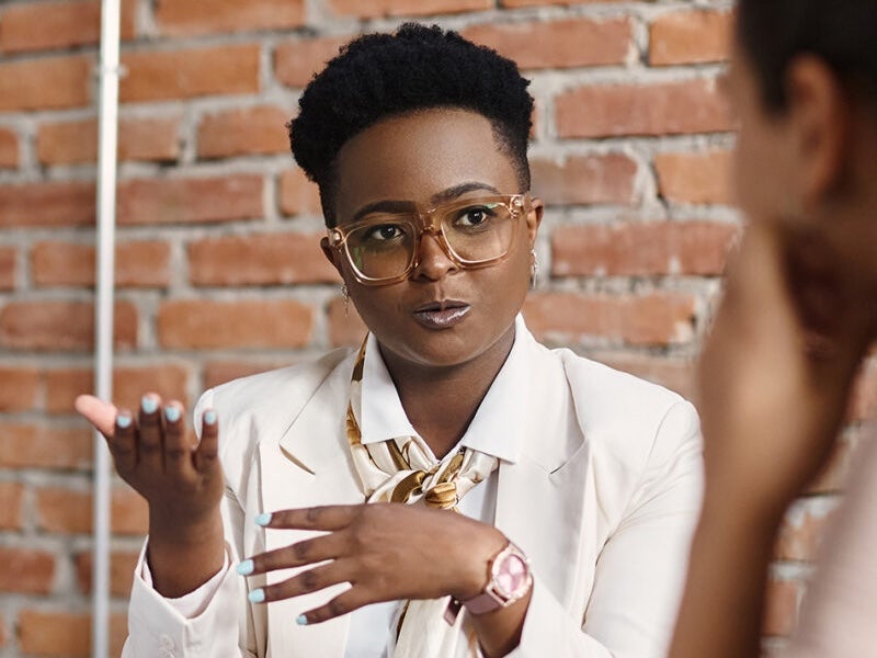 A young professional in glasses explains something to a listening colleague