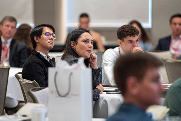 a group of young adults seated at a table, listening attentively.